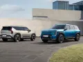 Dwa samochody elektryczne Kia EV9 w kolorach niebieskim i jasnoszarym stoją na zewnątrz.
