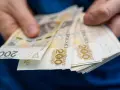 Dłonie trzymające stos banknotów 200 zł. Może to symbolizować zarobki w najlepiej płatnych zawodach.