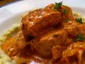 Sabroso pavo en salsa cremosa, adornado con hierbas frescas, servido sobre puré de patatas.
