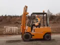 Pomarańczowy wózek widłowy z operatorem w kamizelce odblaskowej przewozi palety.
