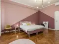 Camera da letto con pareti bicolore, un letto rosa, una sedia gialla e un parquet a spina di pesce. Un esempio di come pitturare una stanza con stile.