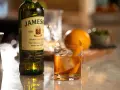 Klasyczny Old Fashioned na bourbonie czy na żytniej whisky? Obok butelka Jameson, szklanka z drinkiem i pomarańcza.