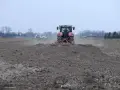 Czerwony traktor z agregatem uprawowym przygotowuje pole pod zasiew. Dzierżawa ziemi w pełni.