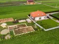 Działka 1000m2 wymiary: rozpoczęta budowa domu, gotowy fundament, sterta cegieł, drewno, żwir, obok stoi dom z pomarańczowym dachem i samochód.