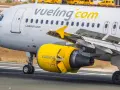 Samolot linii Vueling, hiszpańskie linie lotnicze, z żółtym silnikiem i logo na skrzydle, kołuje po pasie startowym.