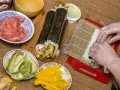 Przygotowanie domowego sushi: ryż, awokado, mango, imbir i rolki w trakcie zwijania.