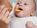 Rączka podaje łyżeczkę z jedzeniem, co dla 6 miesięcznego dziecka jest nowym doświadczeniem.
