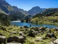Deux randonneurs explorent un sentier rocailleux menant à un lac bleu étincelant, entouré de montagnes majestueuses. Une parfaite randonnée Val d'Aran.