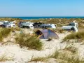 Ein sonniger Campingplatz in Deutschland am Meer. Wohnwagen und Zelte stehen zwischen Dünen und Strandhafer.