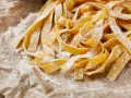 Świeży, domowy makaron tagliatelle, posypany mąką, czeka na gotowanie. Idealny przepis, jak zrobić makaron.