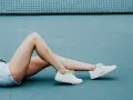 Frau mit blonden Haaren liegt auf blauem Untergrund, trägt Jeansshorts und weiße Sneaker.