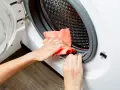 Hands cleaning the rubber seal of a washing machine with an orange cloth. This is part of how to clean washing machine.