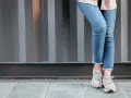 Nogawki jeansów postrzępione na dole, w połączeniu z błyszczącymi sneakersami, tworzą modny look.
