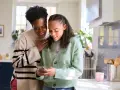 Mère et fille souriantes regardant un téléphone. Une conversation sur la pension alimentaire jusqu'à quel âge.