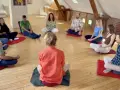 Menschen sitzen im Kreis auf Meditationskissen. Eine Gruppe genießt eine **Auszeit im Kloster**, umgeben von Ruhe und Gemeinschaft.