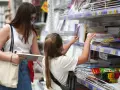 Niña y madre revisan estantes llenos de cuadernos y material escolar.