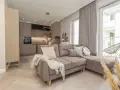 Elegancki salon z aneksem kuchennym w stylu monochromatycznym. Brązowa sofa z poduszkami, jasne drewno na podłodze.