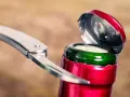 Metalowy widelec próbuje otworzyć butelkę wina, podważając czerwone wieczko.