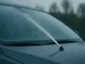 Na mokrej masce samochodu widać strumień powietrza z dyszy spryskiwacza. Pompka spryskiwacza działa, a płyn nie leci.
