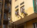 Operai in corda applicano diversi tipi di intonaco per esterni su un edificio giallo.