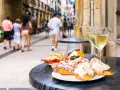 Njut av utsökt san sebastian mat och vitt vin på ett café. Folk promenerar på gatan i bakgrunden.