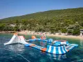 Wodne atrakcje na krystalicznie czystej wodzie, idealne na wakacje w **camping Slatina**. W tle zielone wzgórza i plaża.