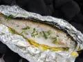 Eine ganze Forelle vom Grill in Alufolie, mit Zitronenscheiben und Rosmarin verfeinert, bereit für den Genuss.
