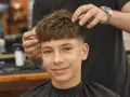 Ein Junge mit einem modernen Haarschnitt, der von einem Friseur gestylt wird. Diese Frisuren für Jungs sind im Trend.
