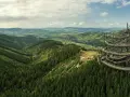 Widok na Sky Walk Czechy, spiralną wieżę widokową pośród zielonych wzgórz i lasów.