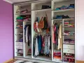 Armadio a muro con ante scorrevoli, pieno di vestiti piegati e appesi, borse e scarpe. Le dimensioni armadio camera da letto sono ben sfruttate.