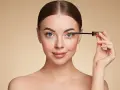 Femme appliquant du mascara sur ses cils, regard bleu intense.