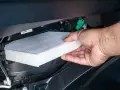 A hand removes a new cabin air filter from its packaging, ready to install it. This shows how to change cabin air filter for cleaner air.