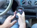 Ręce trzymające skaner diagnostyczny, który pokazuje menu z opcją "02 Sensor Test". Urządzenie może pomóc zdiagnozować problemy z czujnikiem spalania stukowego.