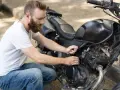 Uomo con barba lavora sul motore di una moto, forse per sostituire subito la batteria.