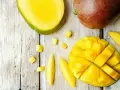 Czy pies może mango? Na drewnianym blacie leżą soczyste kawałki mango, pokrojone w kostkę i paski. Obok całe, dojrzałe owoce.