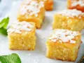 Fette di torta al cocco dorata, guarnite con scaglie di cocco e foglie di menta fresca.