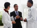 Un uomo in giacca e cravatta parla con due medici in camice bianco. Forse discutono di un nuovo farmaco e del suo informatore scientifico stipendio.