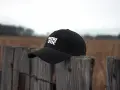 Czarna czapka z daszkiem "PATRIOTIC" na drewnianym płocie. Dowiedz się, jak wyprać czapkę z daszkiem, by wyglądała jak nowa.