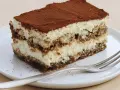 Une part de tiramisu sans oeuf, légère et aérienne, saupoudrée de cacao, sur une assiette blanche avec une fourchette.