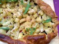 Torta salata patate e cipolle dorata e croccante, guarnita con rucola e peperoncino.