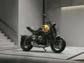 Żółty motocykl Triumph Trident 660 z czarnymi akcentami stoi na betonowej posadzce obok schodów.