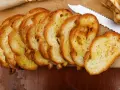 Fette dorate di pane con lievito madre, appena tostato, su un tagliere di legno. Un coltello seghettato è pronto per affettare altro pane.