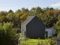 Nowoczesny dom z czarną elewacją w otoczeniu jesiennej zieleni. Minimalistyczna bryła harmonijnie wtapia się w krajobraz.