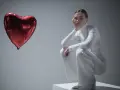 Kobieta w białym stroju siedzi przy czerwonym balonie w kształcie serca, jakby przeżywała zespół Otella.