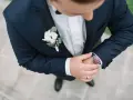 Elegancki pan młody w granatowym garniturze z butonierką co to jest, poprawia zegarek.