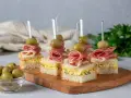 Mini kanapki z szynką, jajkiem i oliwkami na drewnianej desce. Idealne finger food na przyjęcie.
