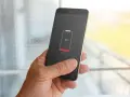 En hand håller en mobil med 3% batteri. Bakgrunden visar suddiga appaktiviteter.