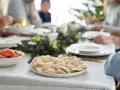 Talerz pierogów i miska z marchewką na wigilijnym stole, w tle rodzina i choinka.
