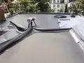Pose d'une membrane d'étanchéité pour l'isolant toit plat. Un ouvrier déroule la bâche noire sur le toit.