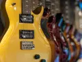 Guitarra eléctrica dorada con pastillas de **single coil** en primer plano, seguida de otras guitarras de colores.